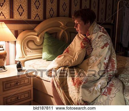 Stock Image - Caucasian man wrapped in blanket on bed. Fotosearch