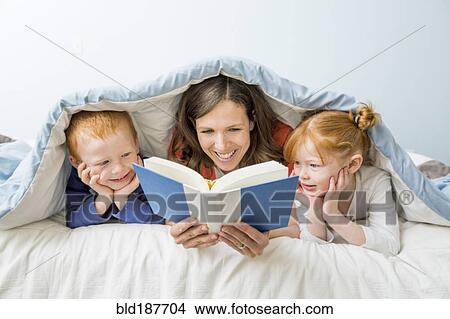 Picture - Caucasian mother and children reading book in bed. Fotosearch