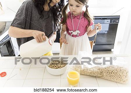 Picture - Caucasian mother and daughter eating cereal in kitchen. Fotosearch