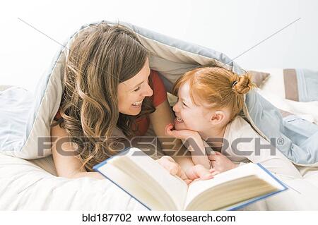 Stock Image - Caucasian mother and daughter reading book in bed. Fotosearch