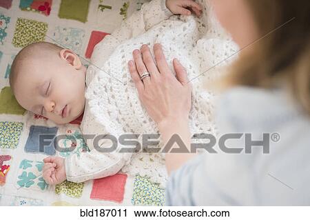 Stock Image - Caucasian mother checking on sleeping baby. Fotosearch