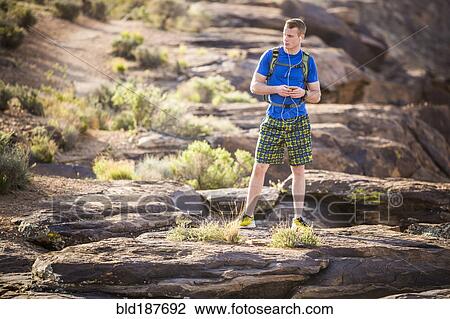 Stock Image - Caucasian teenage boy using cell phone on rock formation. Fotosearch