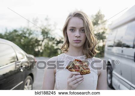 Stock Photography - Caucasian teenage girl eating pizza in parking lot. Fotosearch