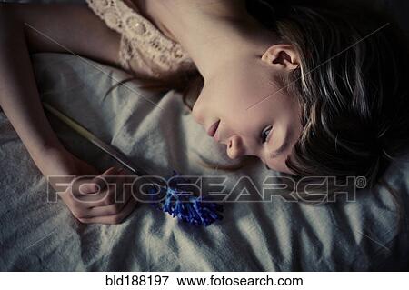 Stock Photo - Caucasian teenage girl holding flower on bed. Fotosearch