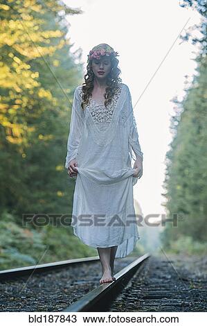 Stock Image - Caucasian woman balancing on train tracks in forest. Fotosearch