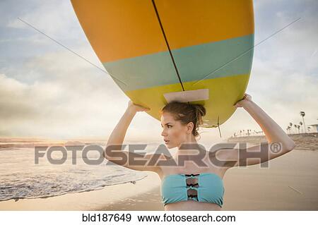 Stock Photo - Caucasian woman carrying surfboard on beach. Fotosearch