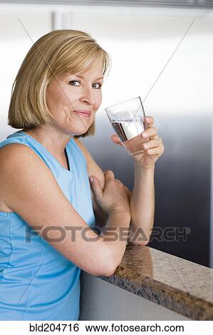Stock Photograph - Caucasian woman drinking water in kitchen. Fotosearch