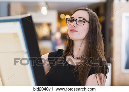 Stock Image - Caucasian woman examining painting in art gallery. Fotosearch