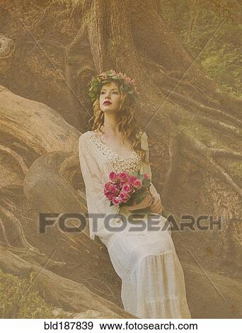 Stock Photo - Caucasian woman holding bouquet of flowers in forest. Fotosearch