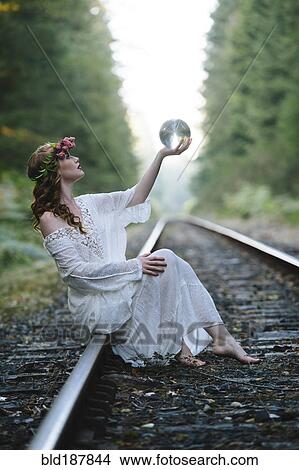 Picture - Caucasian woman holding crystal ball on train tracks. Fotosearch
