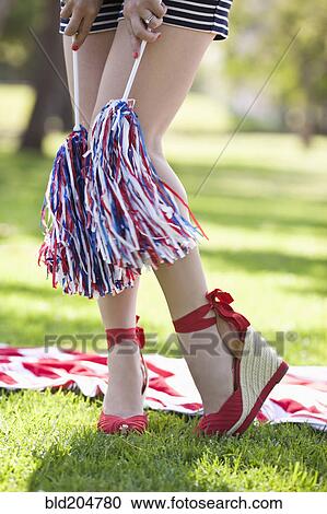 Stock Image - Caucasian woman in heels holding pom-poms. Fotosearch