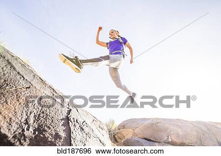 Stock Photograph - Caucasian woman leaping over boulders. Fotosearch