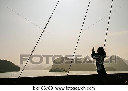 Stock Photo - Caucasian woman photographing rock formations in Ha Long Bay, Vietnam. Fotosearch