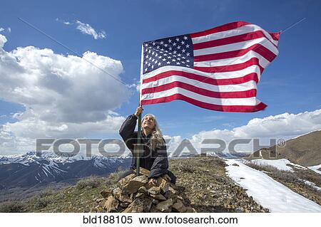 Stock Photography - Caucasian woman planting American flag on remote hilltop. Fotosearch