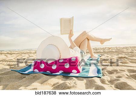 Stock Photo - Caucasian woman reading book on beach. Fotosearch