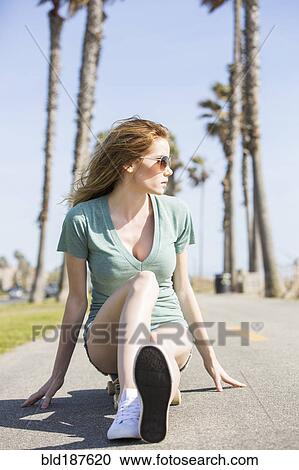 Stock Image - Caucasian woman sitting on skateboard. Fotosearch