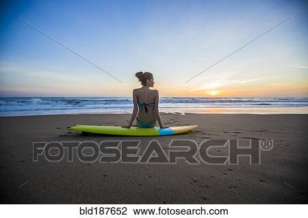 Stock Image - Caucasian woman sitting on surfboard on beach. Fotosearch