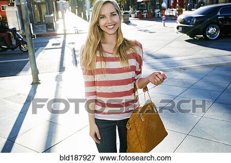 Stock Photo - Caucasian woman smiling on city sidewalk. Fotosearch