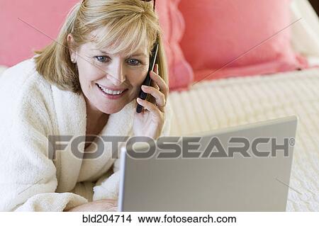 Picture - Caucasian woman talking on cell phone on bed. Fotosearch