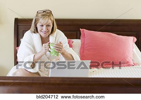 Stock Image - Caucasian woman using laptop on bed. Fotosearch