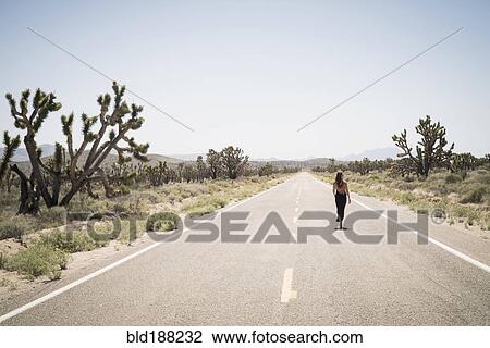 Stock Image - Caucasian woman walking on remote desert road. Fotosearch