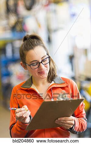 Stock Image - Caucasian woman with clipboard in bicycle shop. Fotosearch