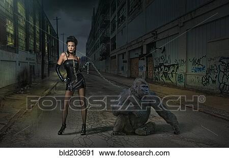 Stock Image - Caucasian woman with gorilla on chain on city street. Fotosearch