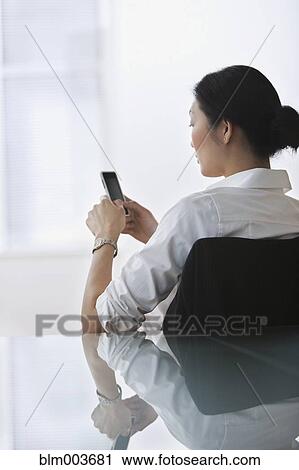 Stock Image - Chinese businesswoman text messaging with cell phone. Fotosearch