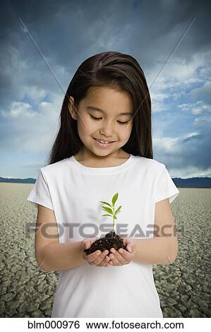 Stock Photograph - Chinese girl holding seedling in desert. Fotosearch