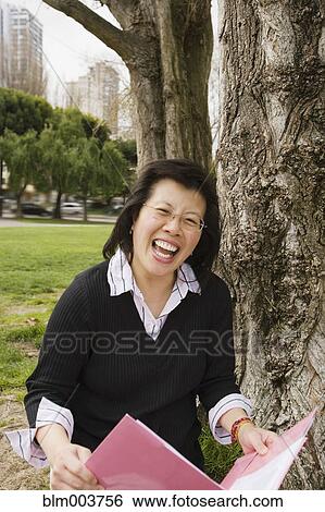 Chinese woman holding folder next to tree View Large Photo Image Stock Photograph - Chinese woman holding folder next to tree. Fotosearch