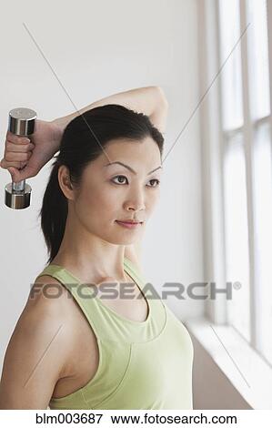 Stock Photo - Chinese woman holding hand weight behind head. Fotosearch