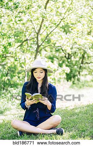 Stock Image - Chinese woman reading in garden. Fotosearch