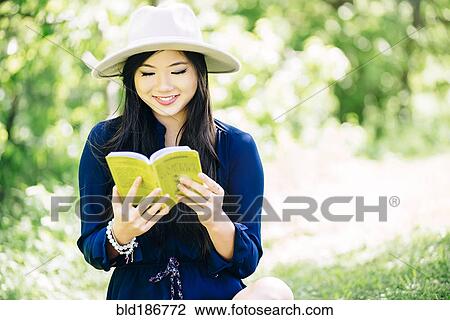 Stock Image - Chinese woman reading in garden. Fotosearch