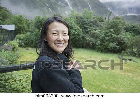 Stock Image - Chinese woman standing on balcony in remote area. Fotosearch