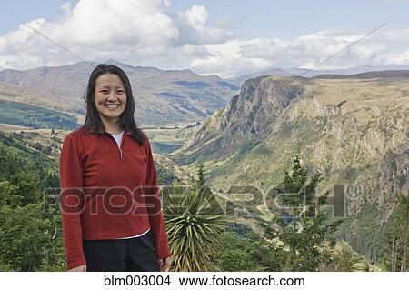 Picture - Chinese woman standing on hilltop with remote valley in distance. Fotosearch