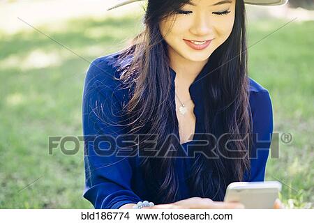 Picture - Chinese woman using cell phone outdoors. Fotosearch