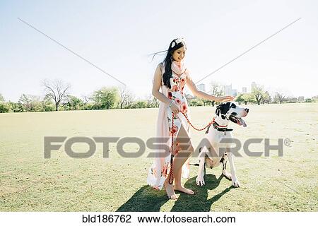 Stock Image - Chinese woman walking dog in field. Fotosearch