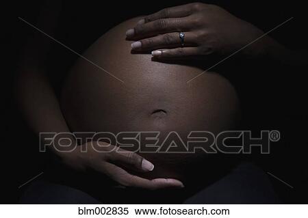 Stock Photography - Close up of mixed race woman's pregnant stomach. Fotosearch