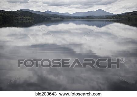 Stock Image - Cloudy sky reflected in still rural lake. Fotosearch