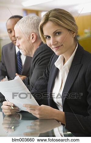 Stock Image - Confident businesswoman holding paperwork in meeting. Fotosearch