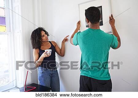 Couple hanging picture in new apartment View Large Photo Image Picture - Couple hanging picture in new apartment. Fotosearch