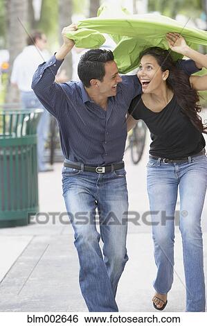Stock Photograph - Couple holding raincoat over heads. Fotosearch
