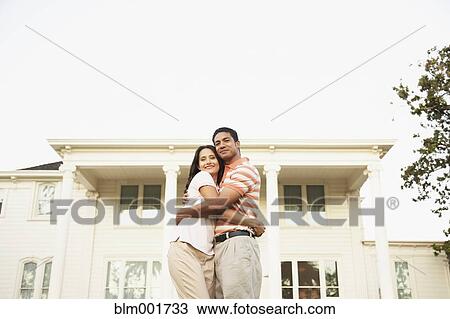 Stock Image - Couple hugging in front of house. Fotosearch