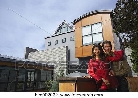 Stock Image - Couple hugging in front of modern house. Fotosearch