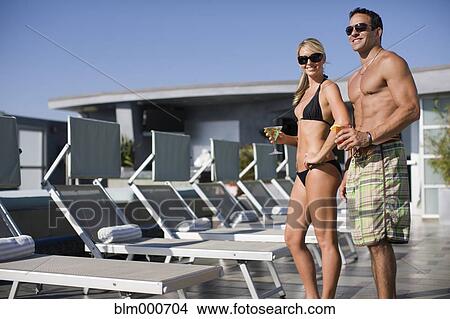 Picture - Couple in bathing suits drinking martinis at poolside. Fotosearch