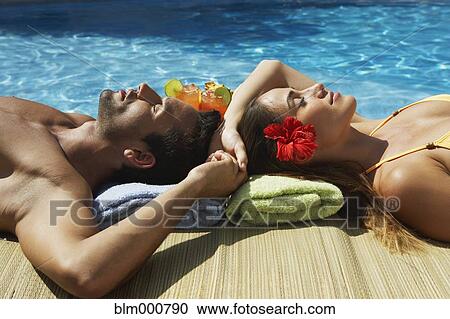 Stock Image - Couple relaxing at edge of swimming pool. Fotosearch