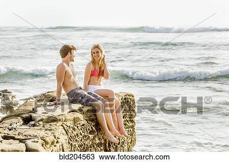 Couple relaxing on rocky beach View Large Photo Image Stock Image - Couple relaxing on rocky beach. Fotosearch