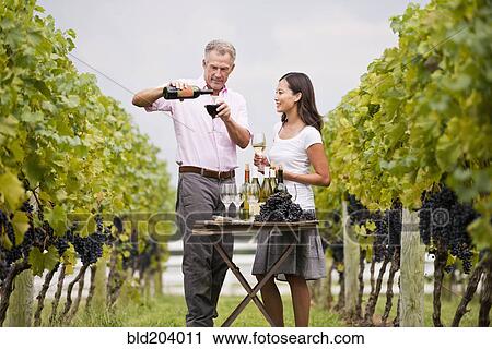 Stock Image - Couple tasting wine together in vineyard. Fotosearch