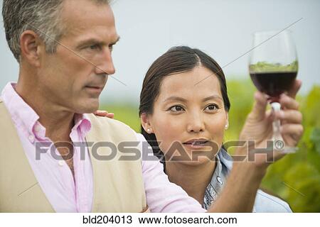 Stock Image - Couple tasting wine together in vineyard. Fotosearch