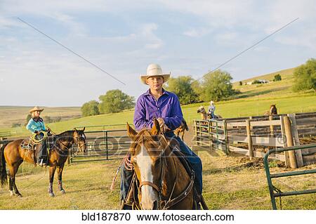 Stock Image - Cowboy riding horseback on ranch. Fotosearch